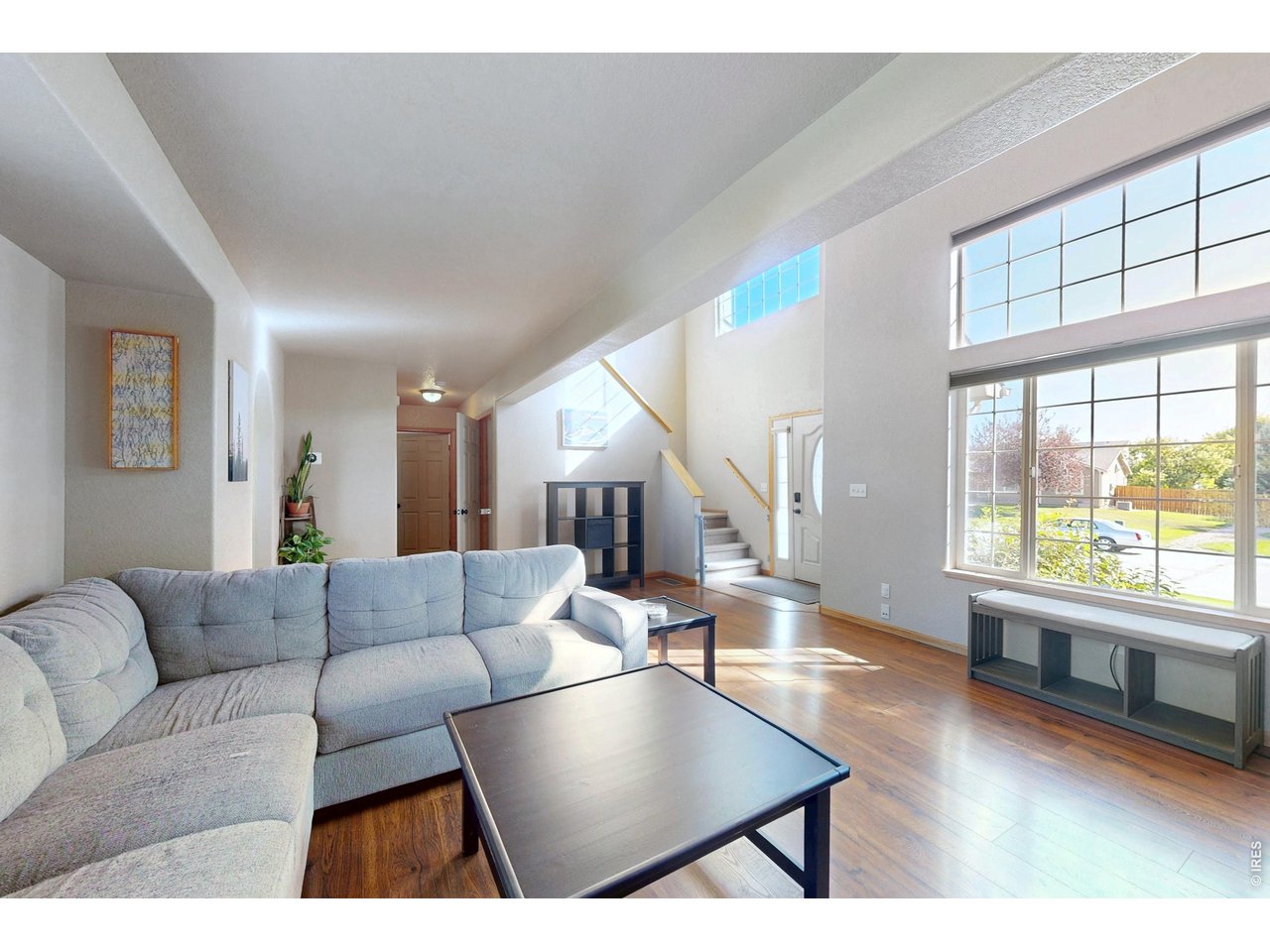 Living room with a gray sectional, hardwood floors, staircase, and tall grid windows.