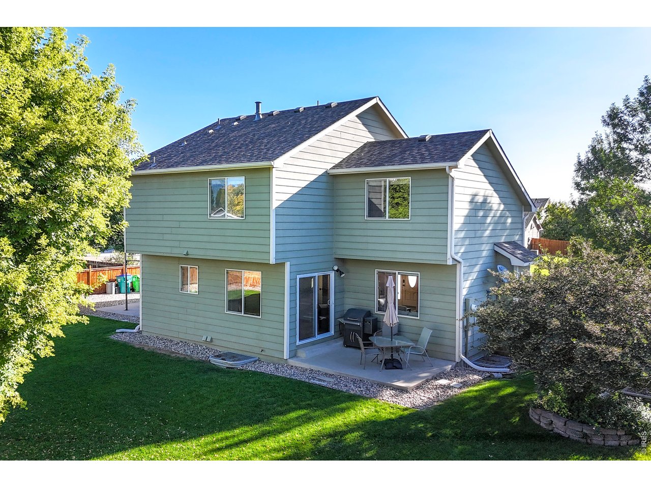 Rear of a sage-green two-story house with a patio, grill, and lawn.