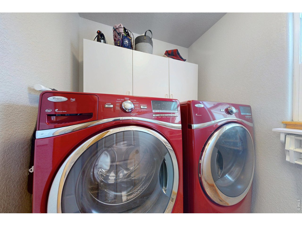 Laundry room with red front-loading washer and dryer beneath white storage cabinets.