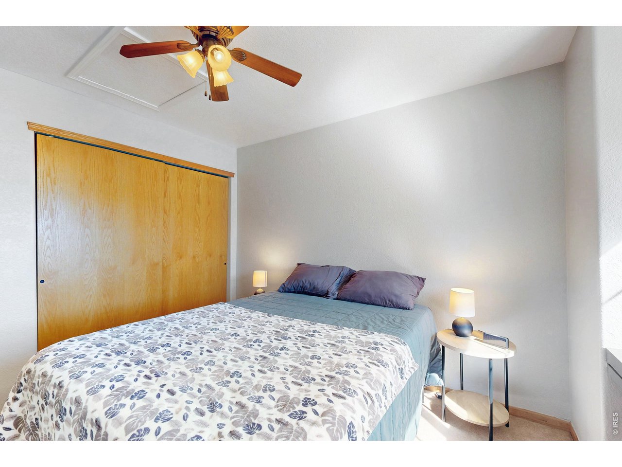 Bedroom with a patterned bedspread, sliding wood closet doors, and a ceiling fan.
