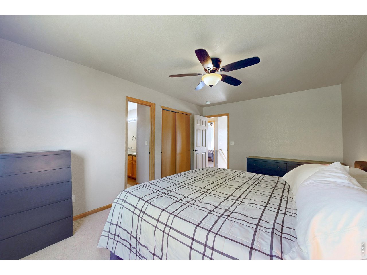 Bedroom with a grid-patterned bedspread, ceiling fan, and doorways to a bathroom and hallway.