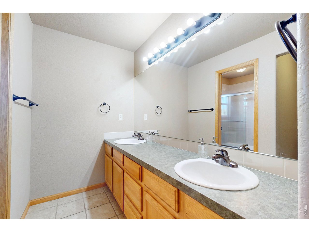 Bathroom with a long double-sink vanity, large mirror, and tiled shower visible in the reflection.