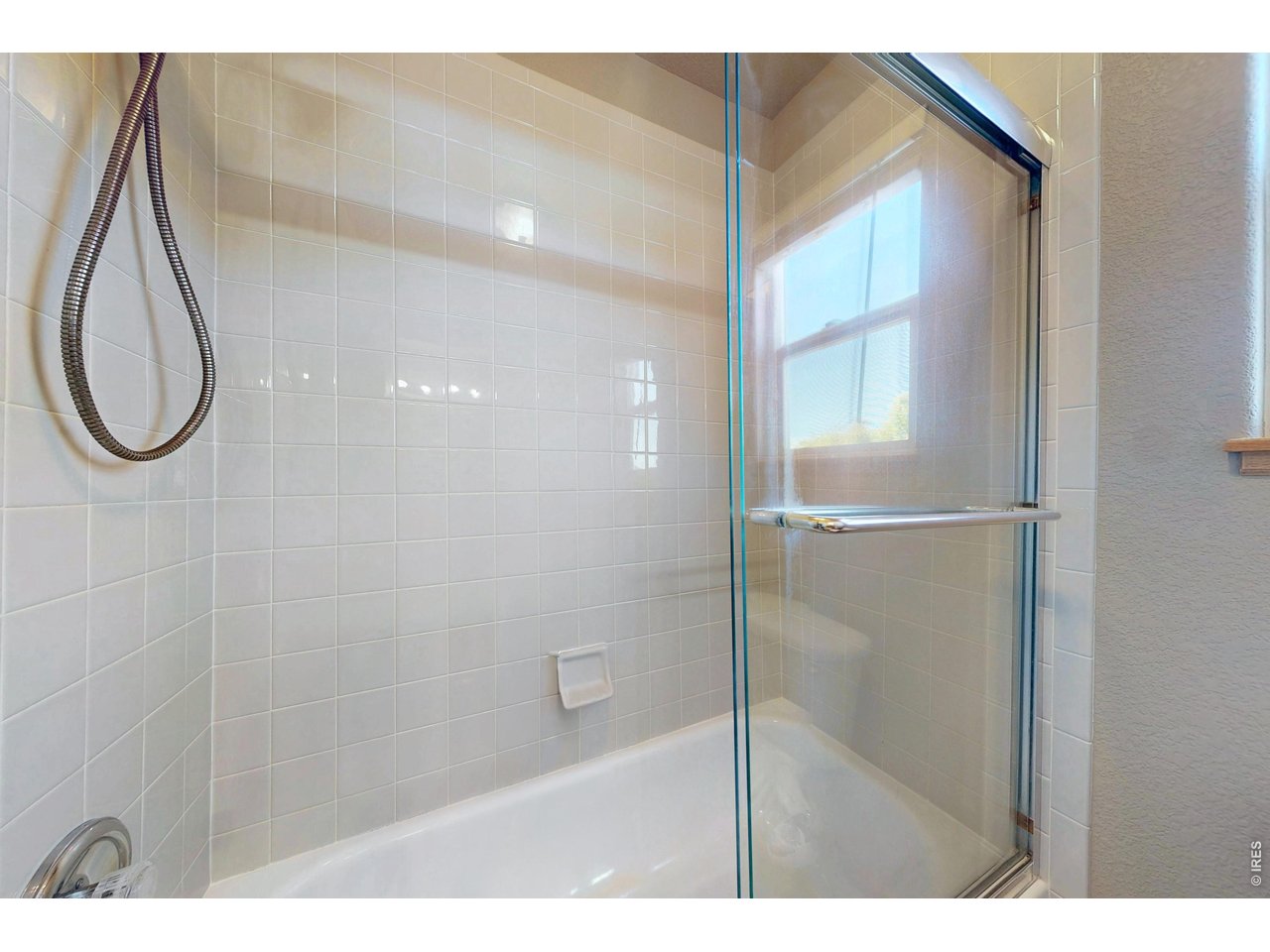 Tiled bathtub and shower with a clear glass enclosure and handheld showerhead.