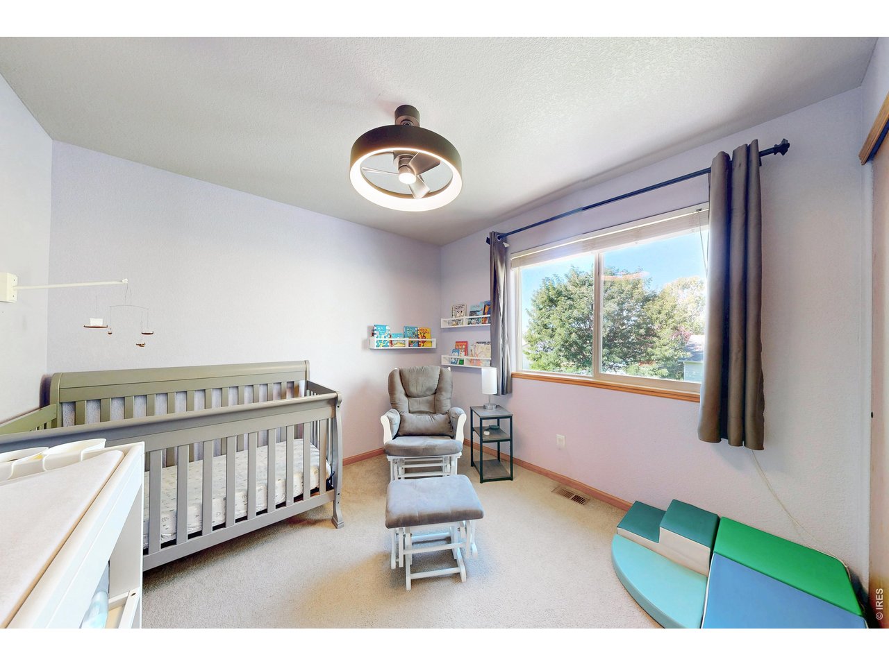 Nursery with a gray crib, rocking chair, and large curtained window.