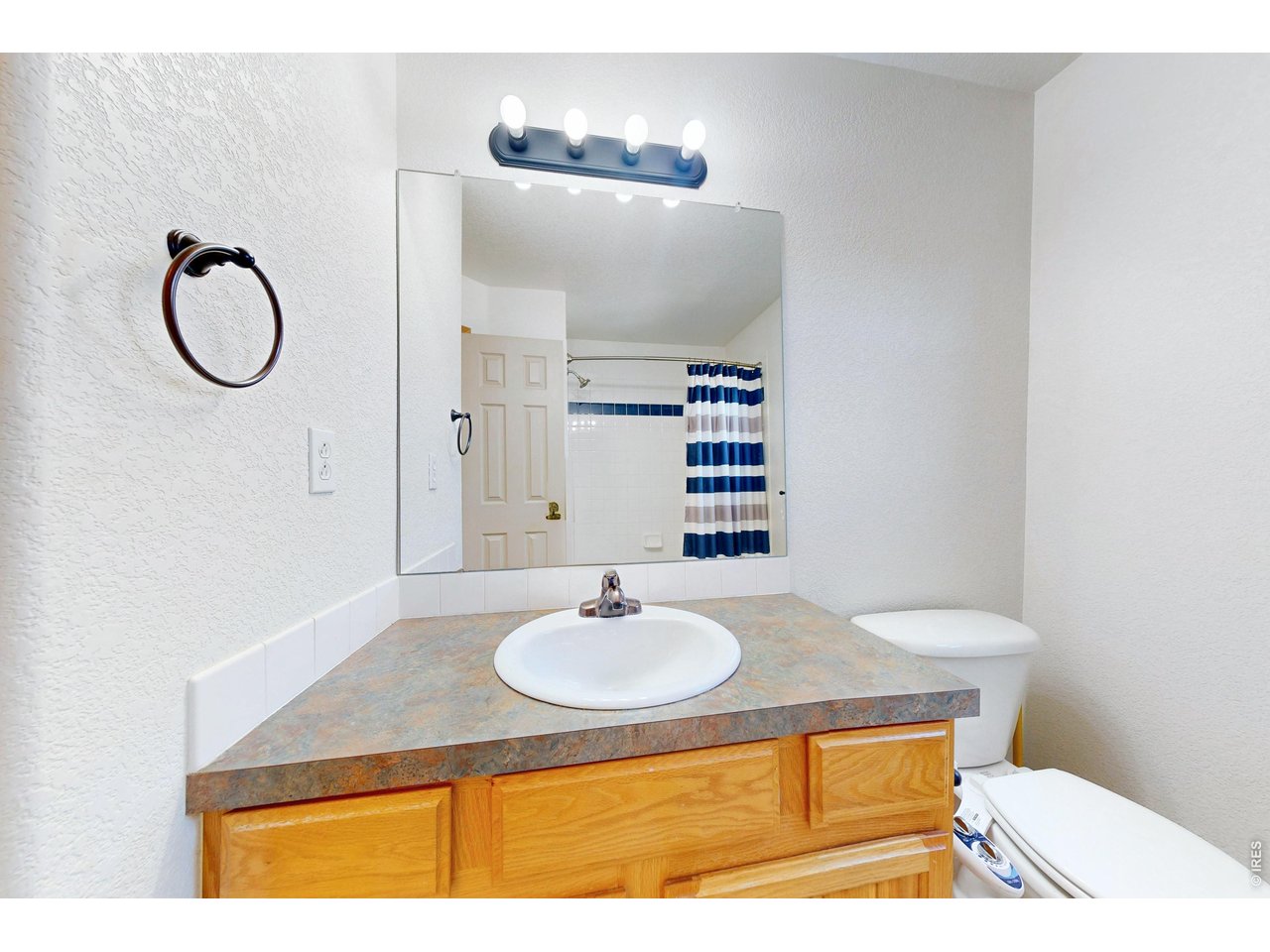 Bathroom with a wood vanity and oval sink, large mirror, and blue-and-white striped shower curtain.