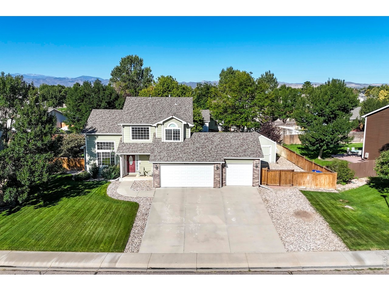 Two-story house with a red front door, three-car garage, landscaped lawn, and distant mountains.