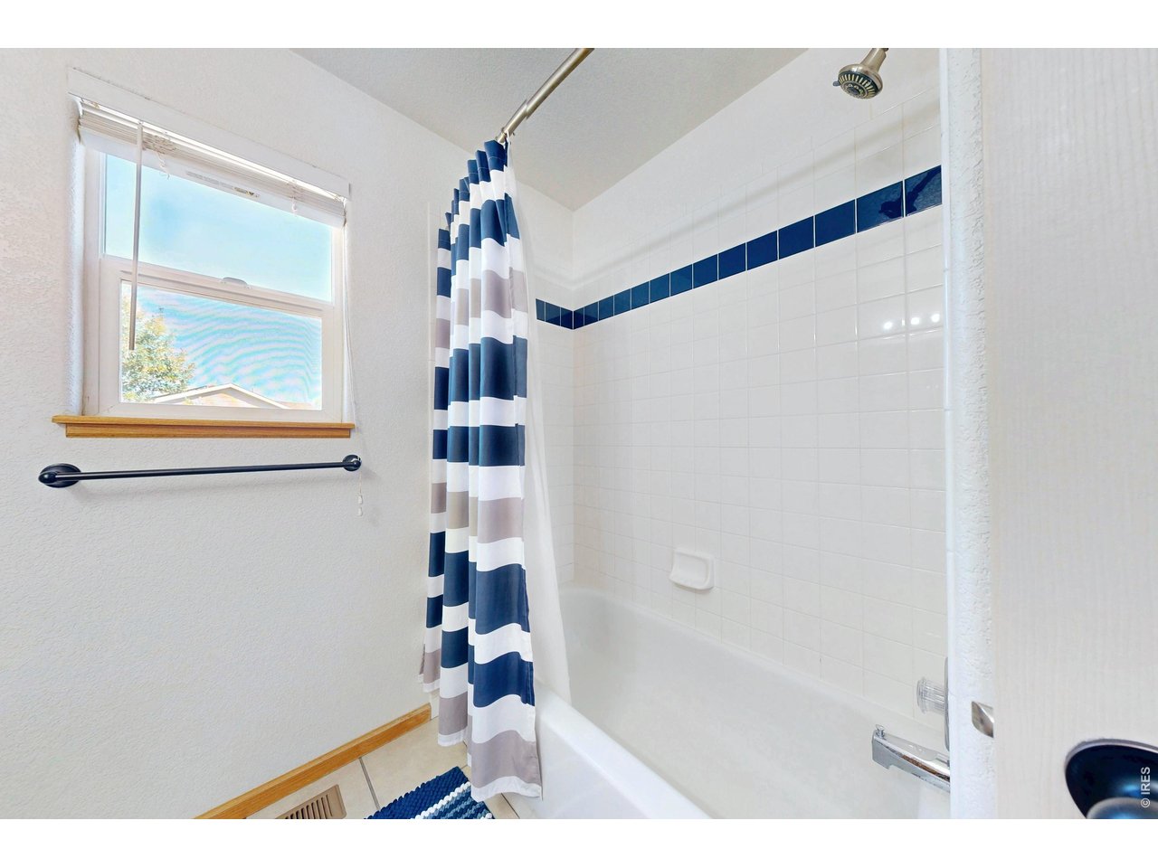 Bathroom with a white tiled tub and shower, navy accent tiles, and a striped blue-and-white curtain.