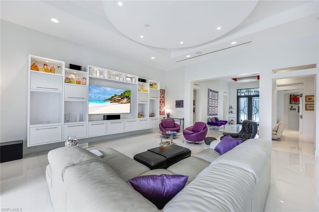 Modern living room with a built-in media wall, white sectional, and purple accent chairs.