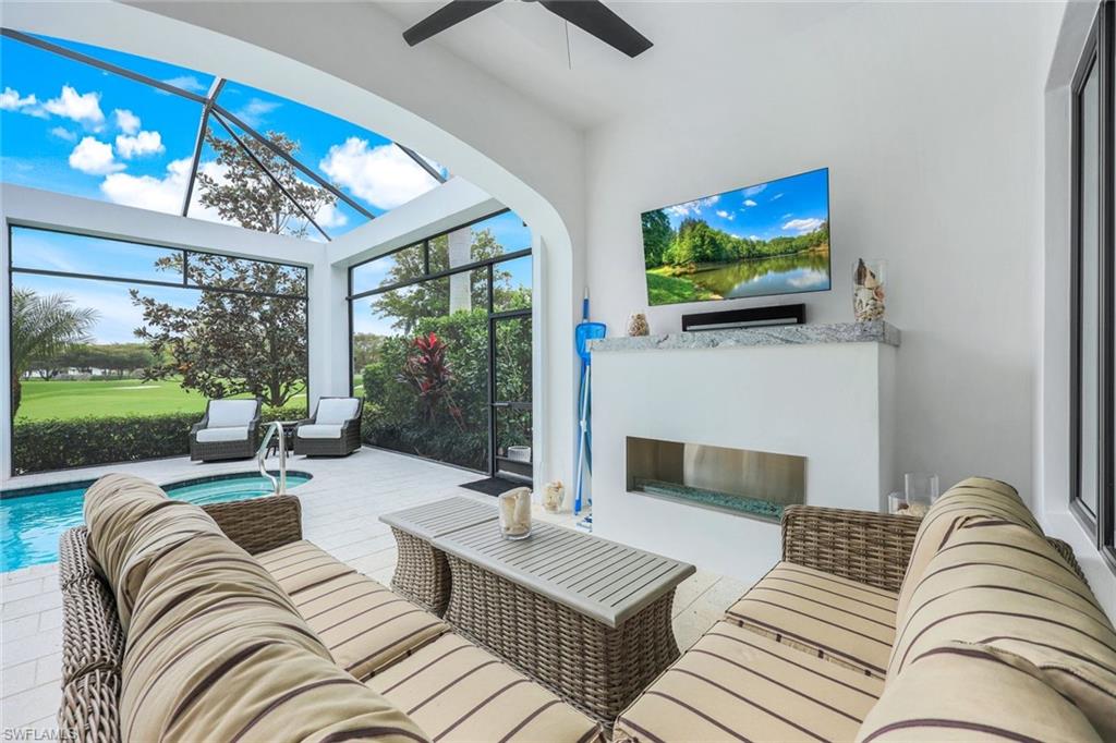 Covered lanai with wicker seating and fireplace, opening to a pool and golf course view.
