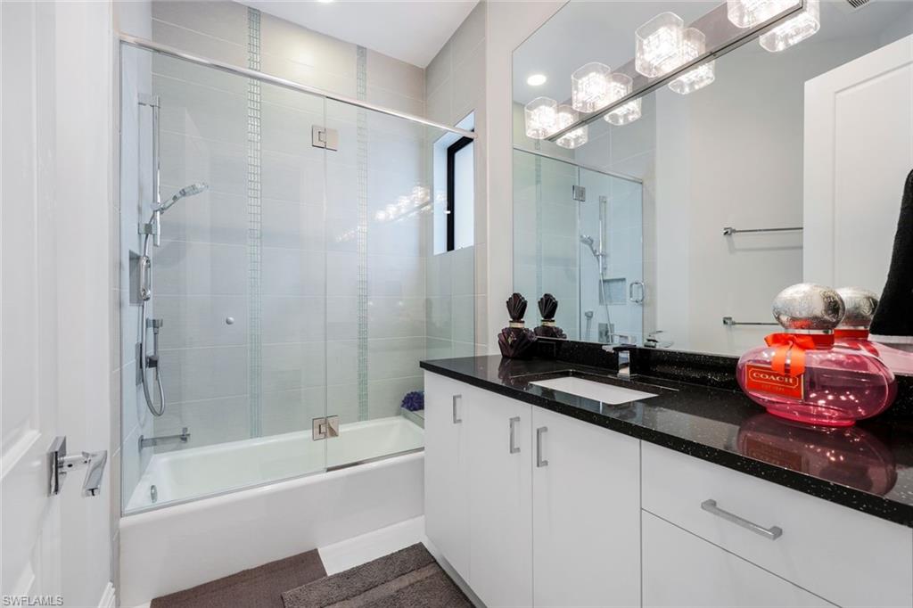 Modern bathroom with a glass-enclosed tub and shower, white vanity, and black countertop.