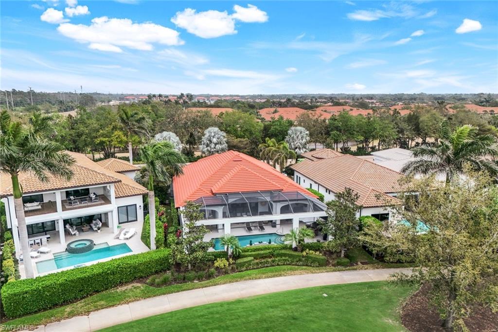 Aerial view of homes with palm-lined yards and pools, including a red-roofed home with a screened enclosure.