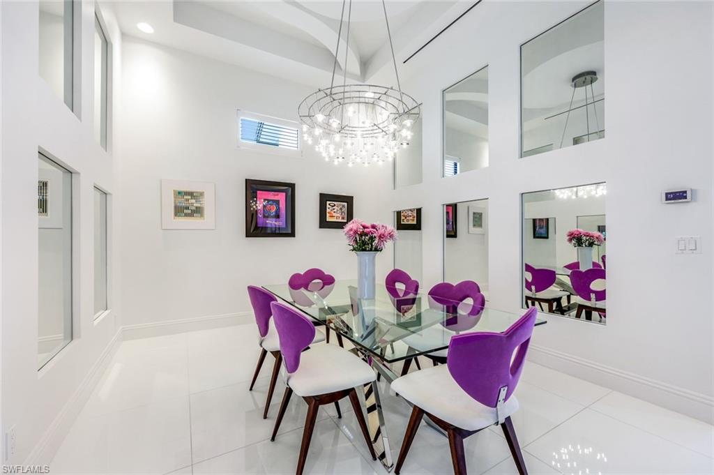 Dining room with a glass table, purple chairs, mirrored walls, and a modern chandelier.