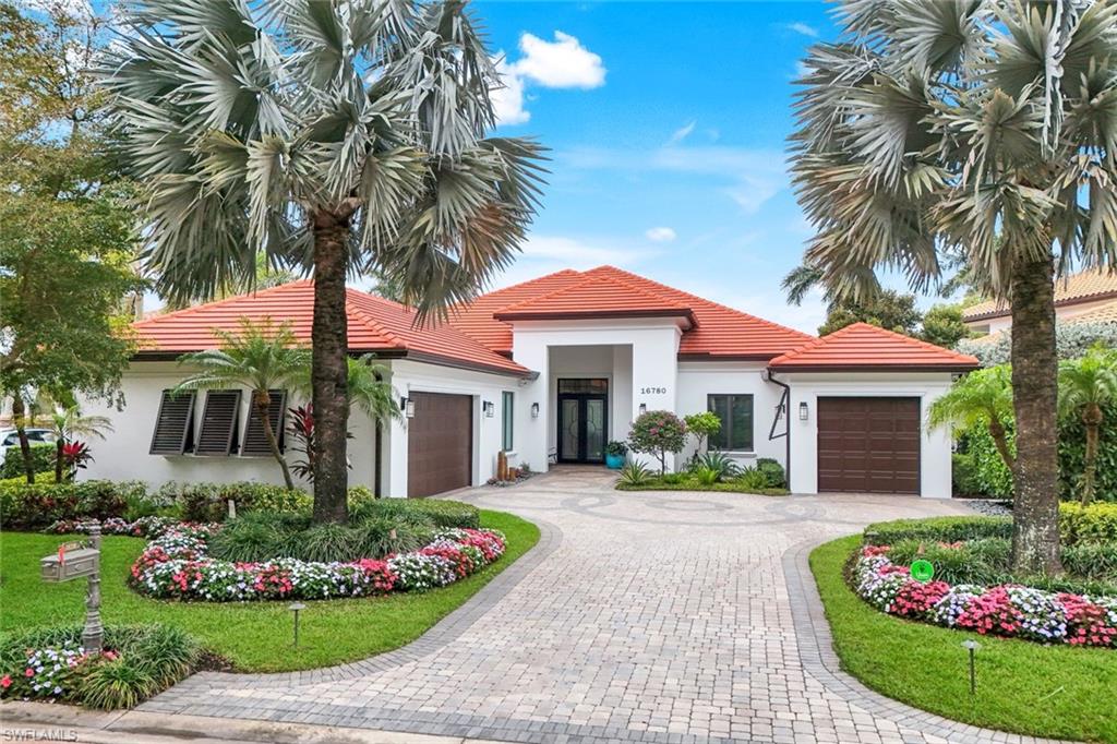 White home with a red tile roof, two garage doors, and a landscaped curved paver driveway.
