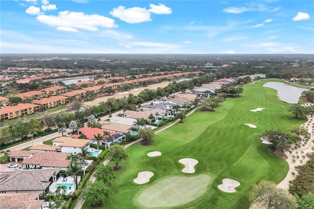 Aerial view of a golf course beside homes with tiled roofs and swimming pools.