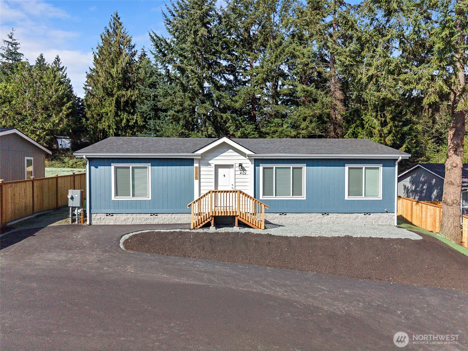 Blue single-story home with white trim, wooden entry steps, and a broad paved driveway.