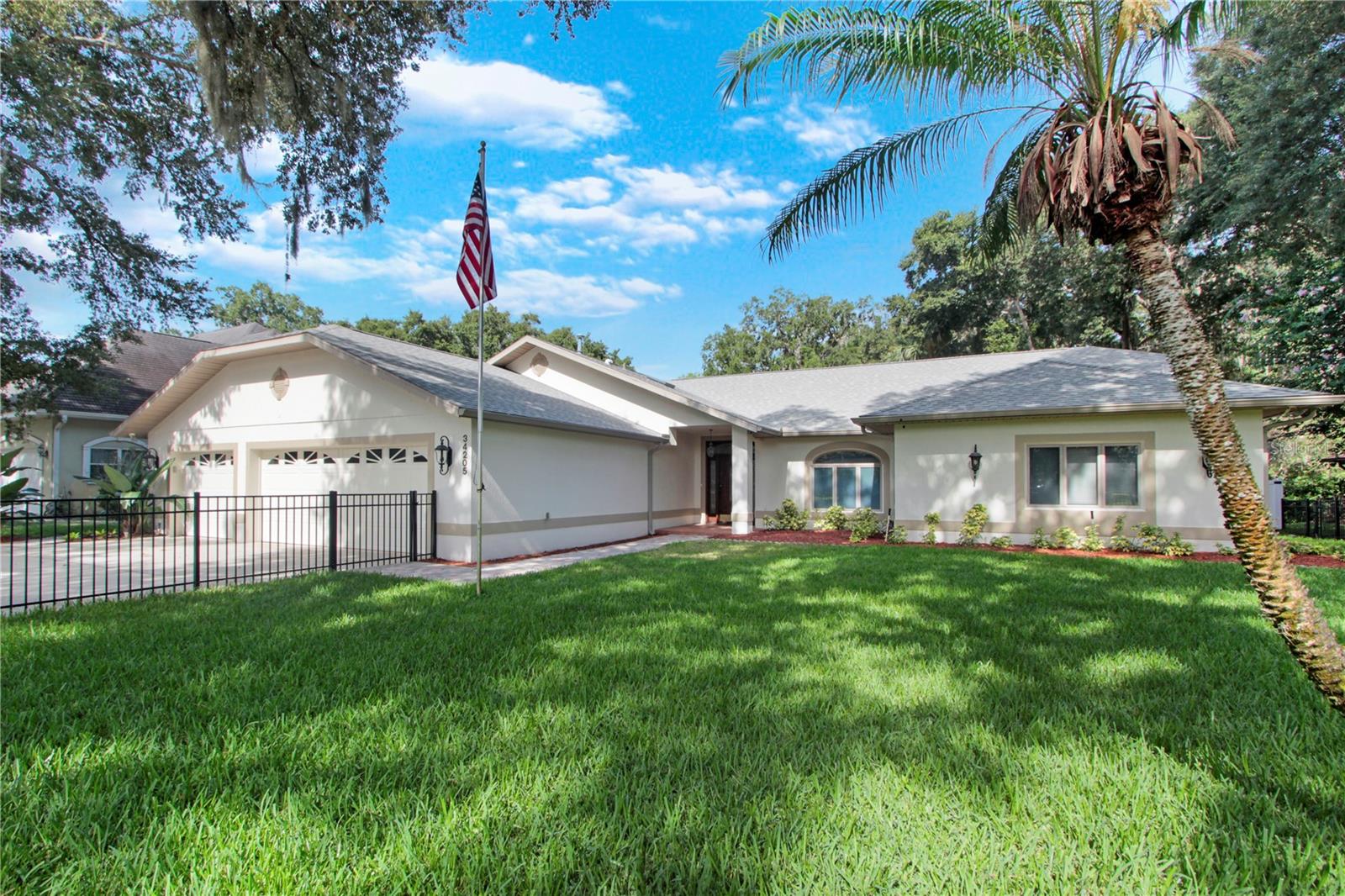 Single-story home with an attached two-car garage, black fence, green lawn, and American flag.