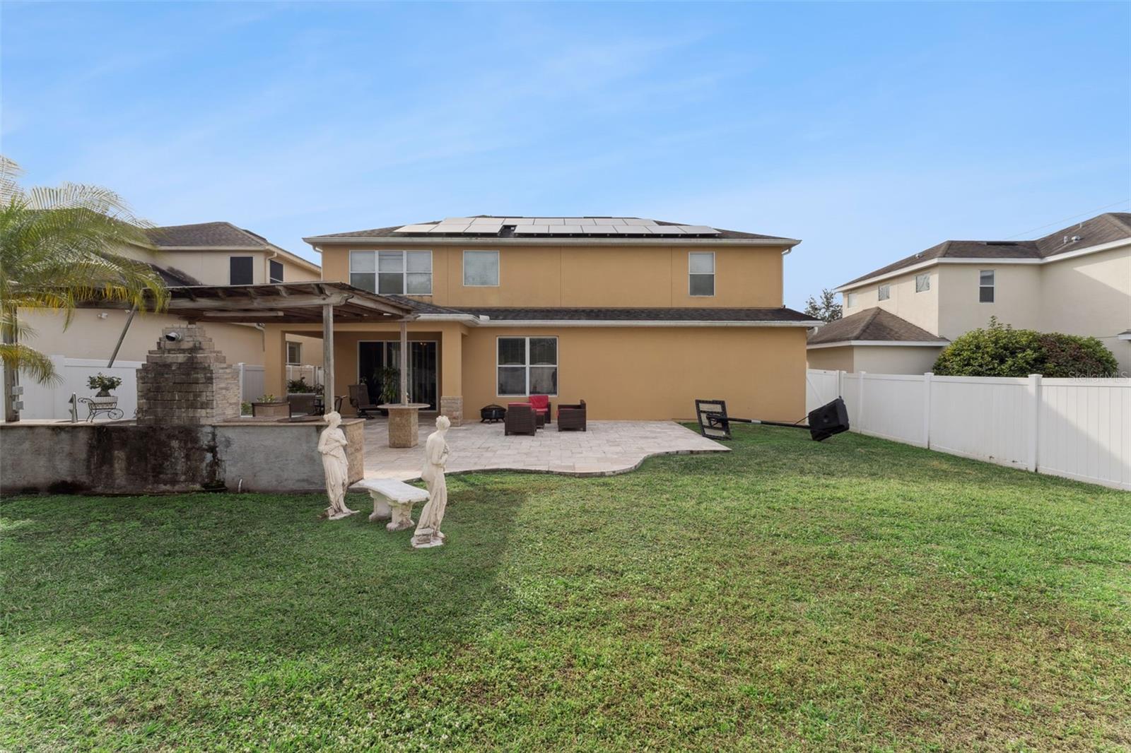 Two-story tan home with rooftop solar panels, a covered patio, and a fenced lawn.