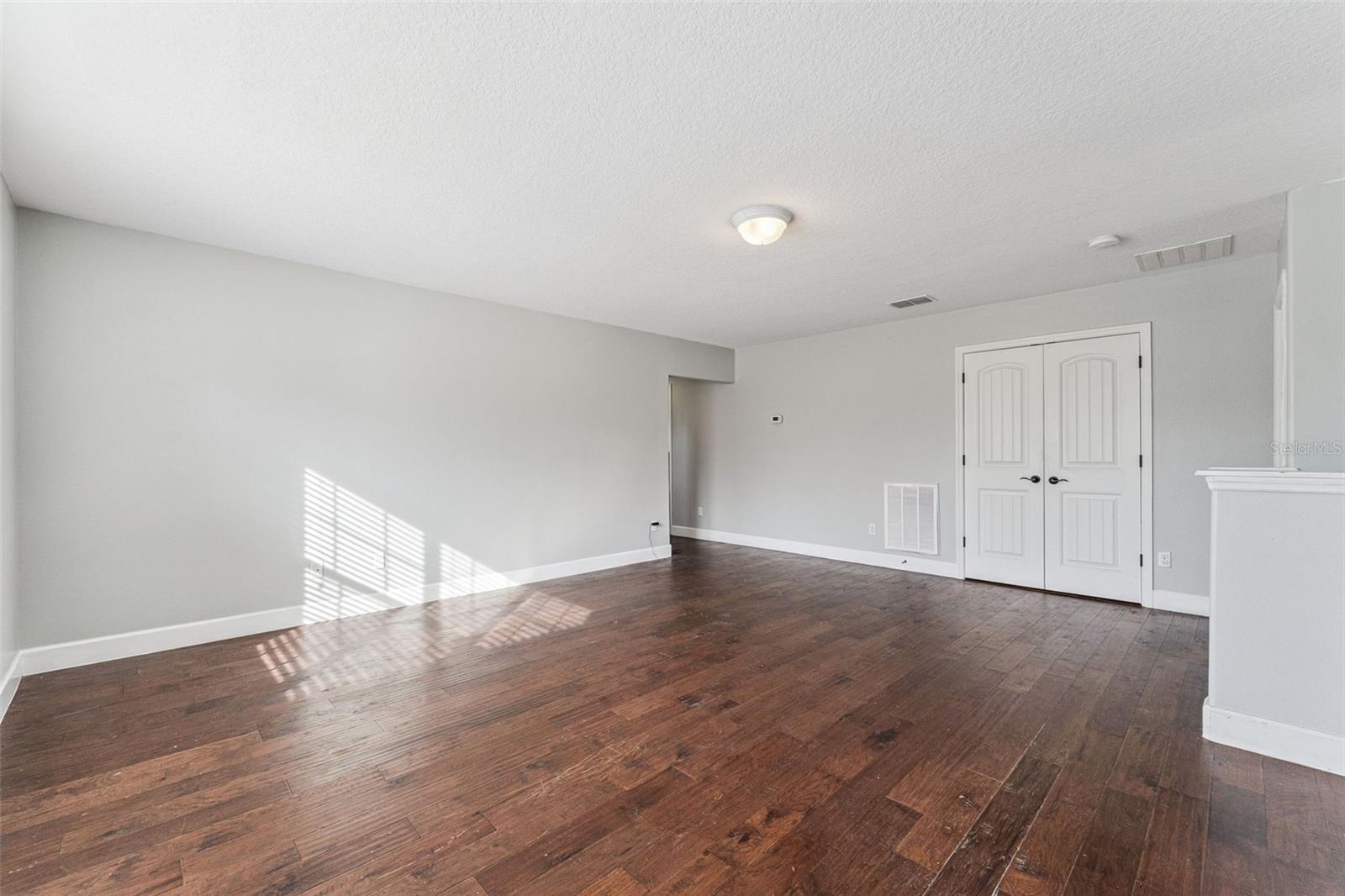 Empty room with dark wood floors, white double doors, and sunlight cast through blinds.