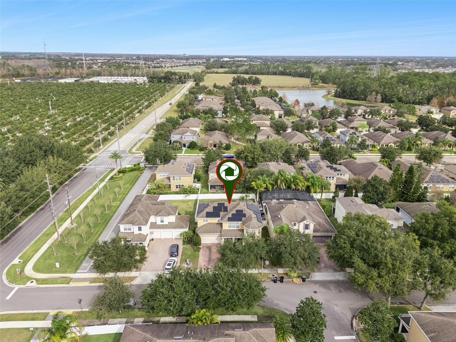 Aerial view of the marked home among neighboring houses, with a pond and planted field nearby.