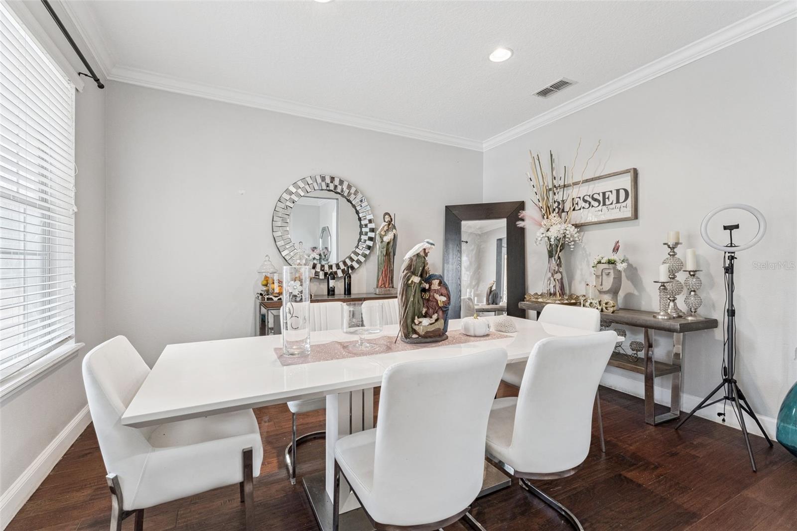 Dining room with a white table, upholstered chairs, dark wood floors, and a mirrored wall accent.