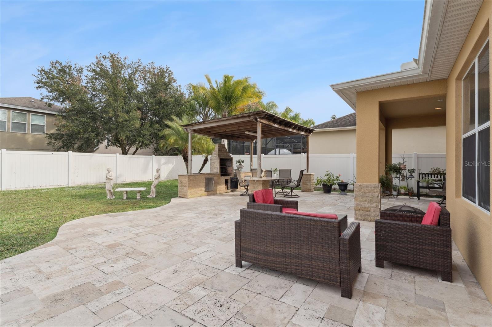 Backyard patio with stone pavers, red-cushioned wicker seating, and a covered outdoor kitchen.