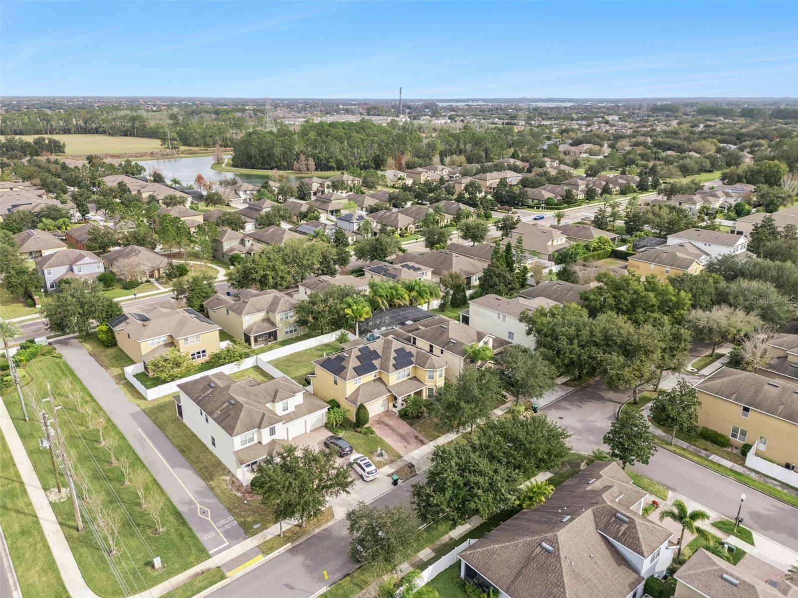 Aerial view of a suburban neighborhood with tree-lined streets and a pond in the distance.