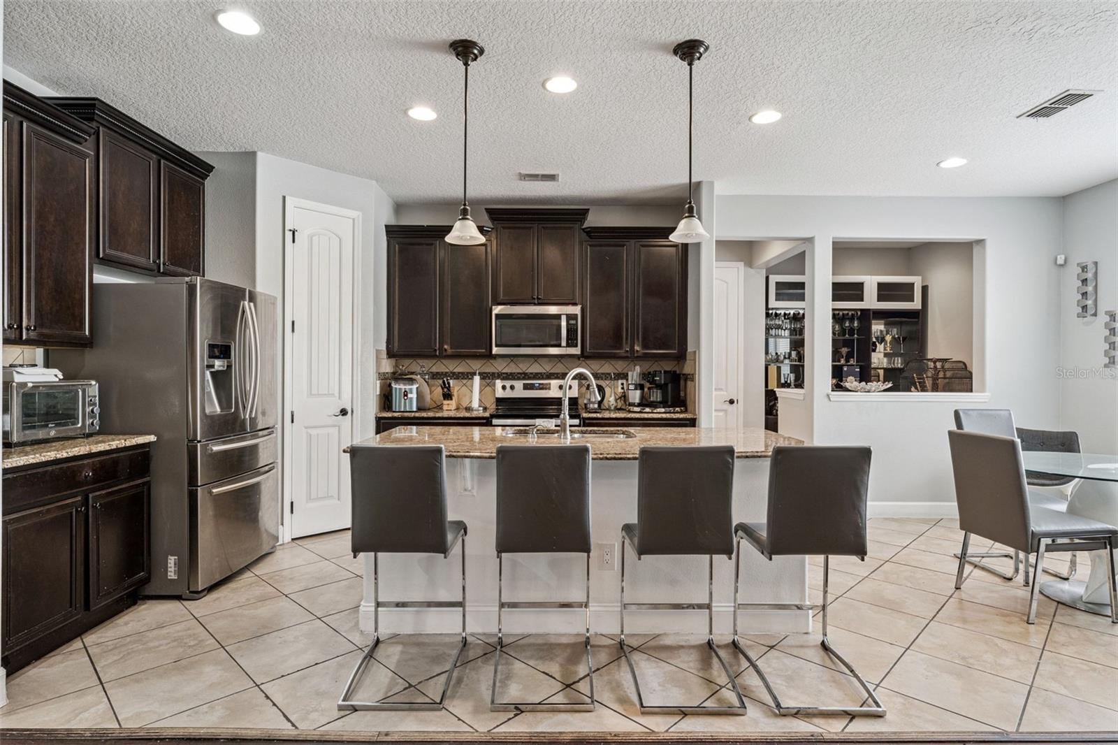 Kitchen with dark wood cabinets, stainless appliances, and a stone island with four bar stools.