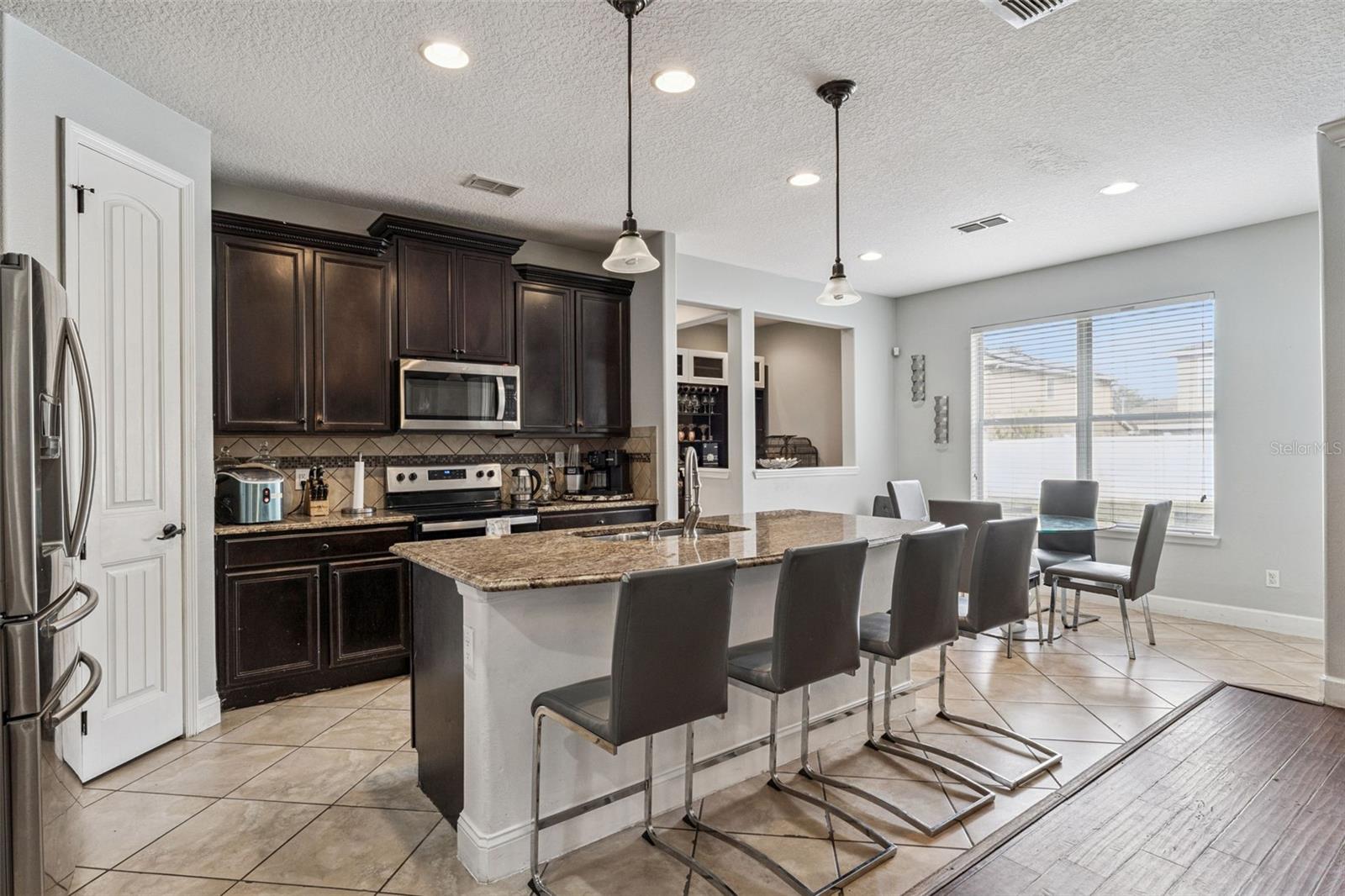 Kitchen with dark cabinets, stainless steel appliances, and a granite island lined with bar stools.