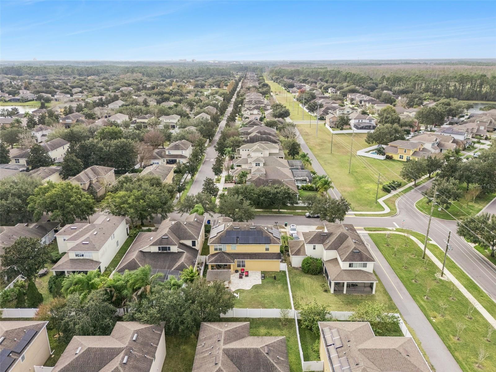 Aerial neighborhood view with a yellow home featuring rooftop solar panels and a fenced backyard.