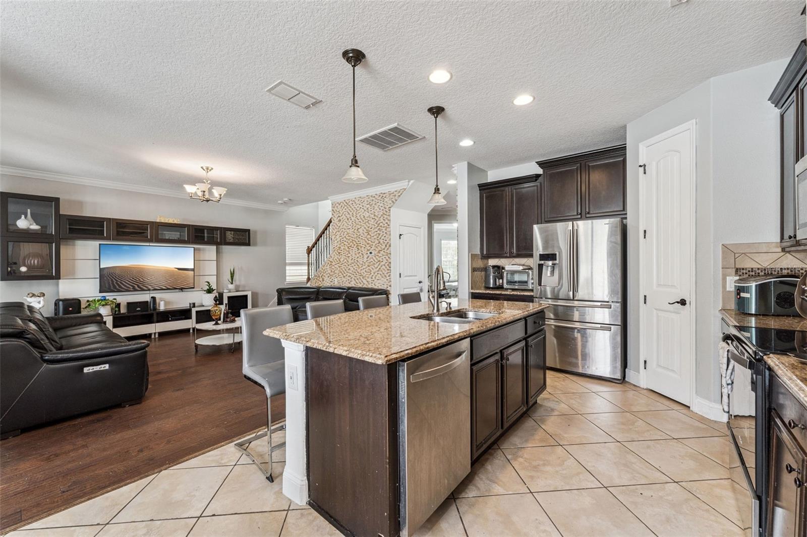 Open-plan kitchen with granite island and stainless appliances adjoining a living room with a black leather sectional.