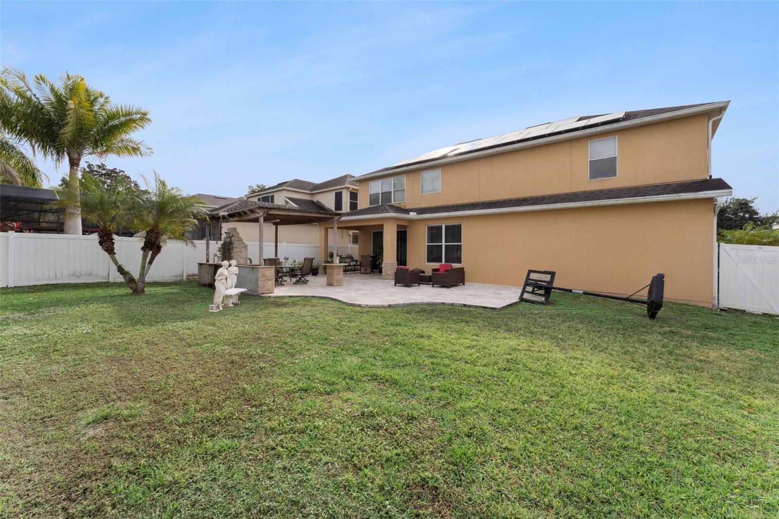 Two-story tan home with solar panels and a covered patio opening onto a fenced lawn.