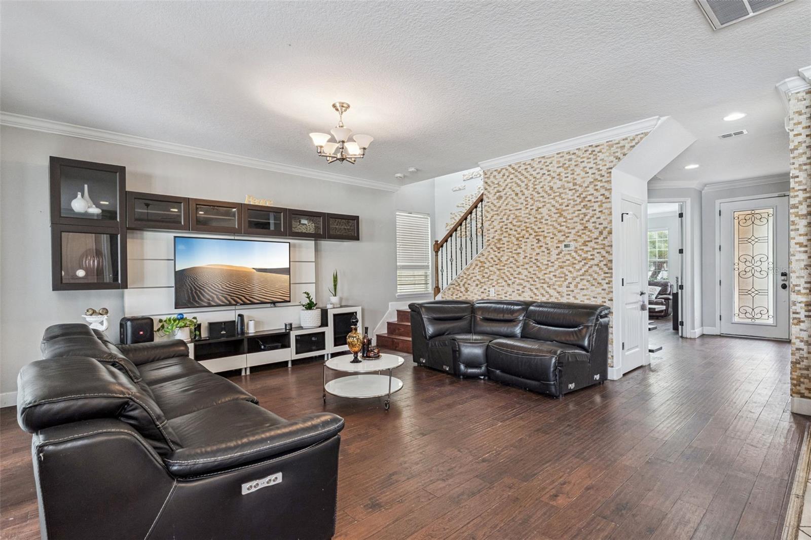 Living room with black leather sofas, a wall-mounted television, and a mosaic-tile staircase wall.