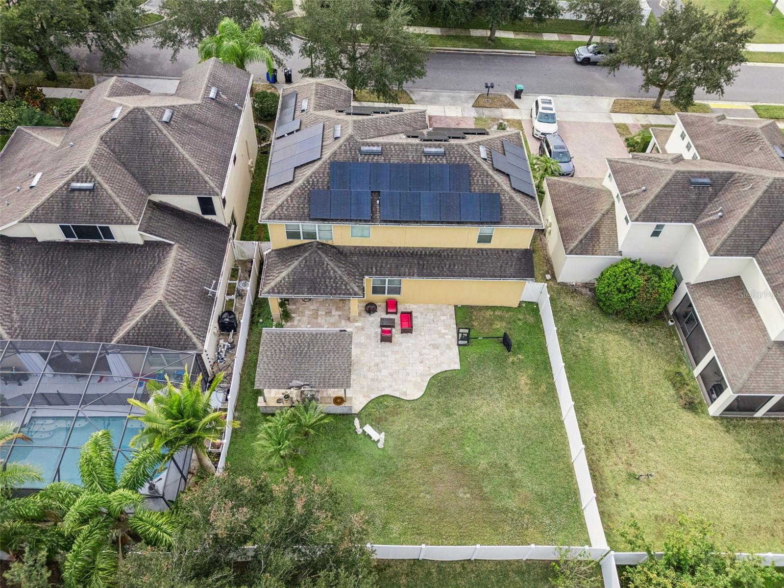 Aerial view of a solar-paneled home with a fenced lawn and stone patio.