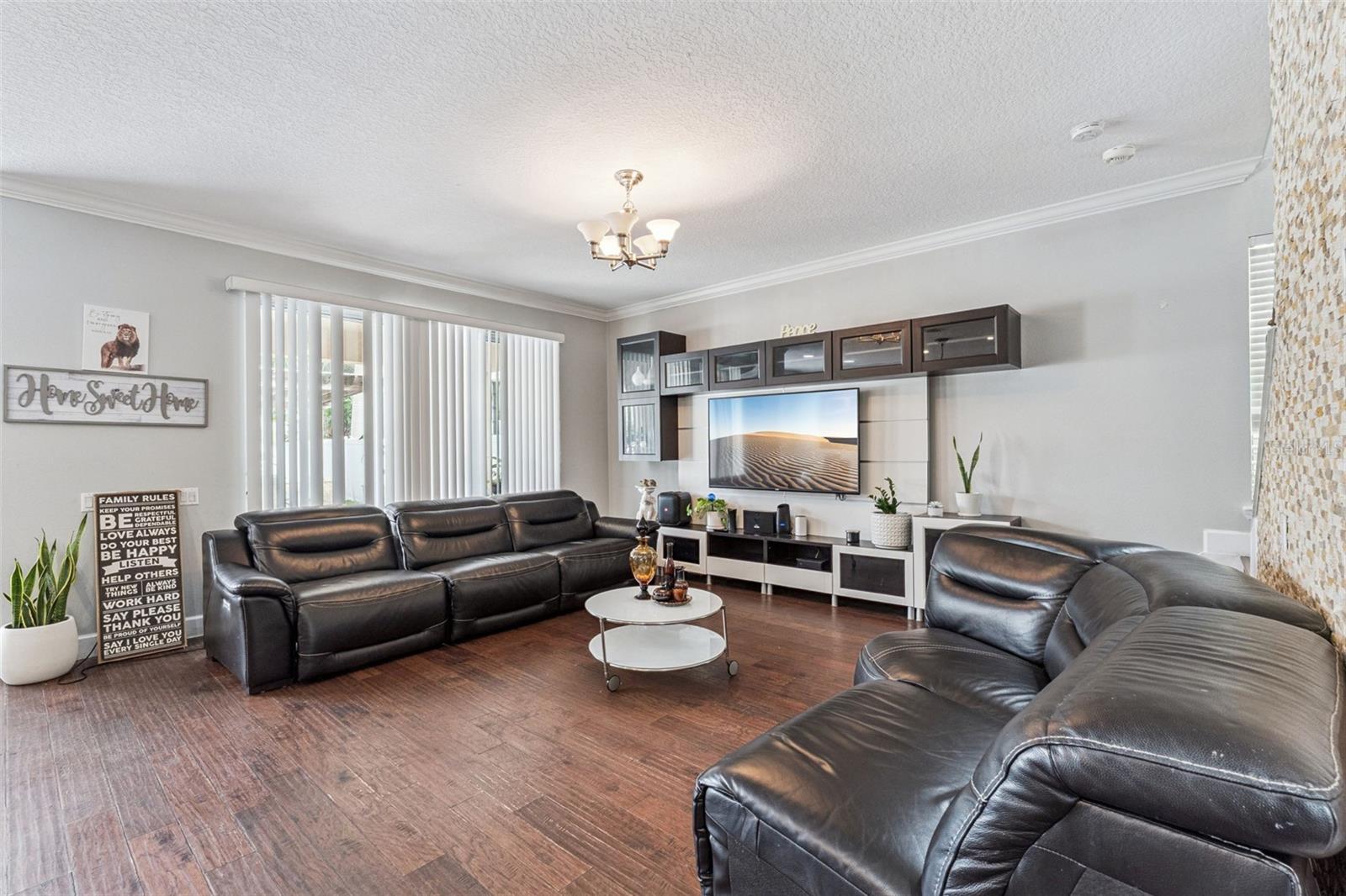 Furnished living room with dark leather sofas, hardwood floors, and a wall-mounted TV.