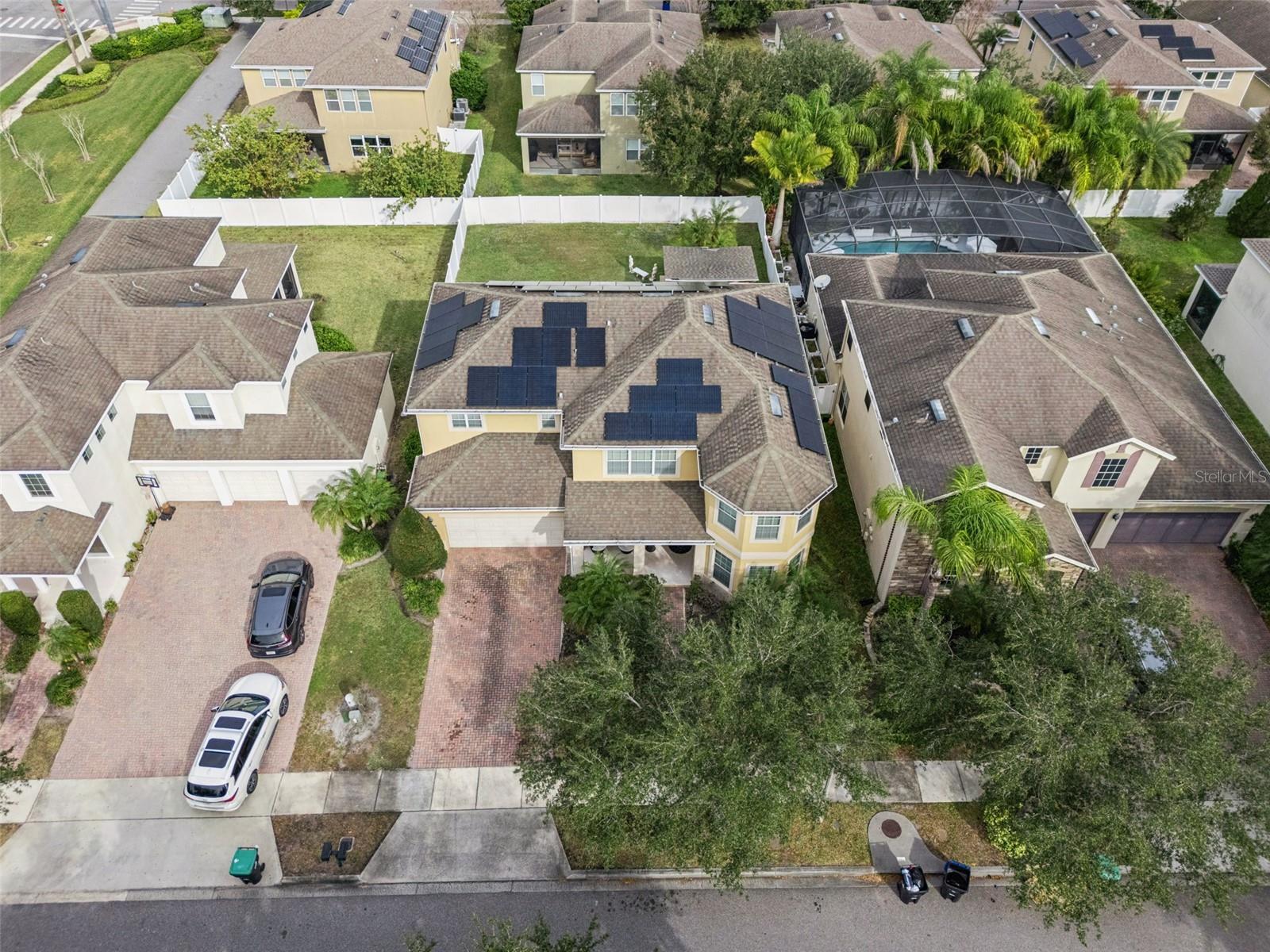 Aerial view of a two-story home with rooftop solar panels and a fenced backyard.