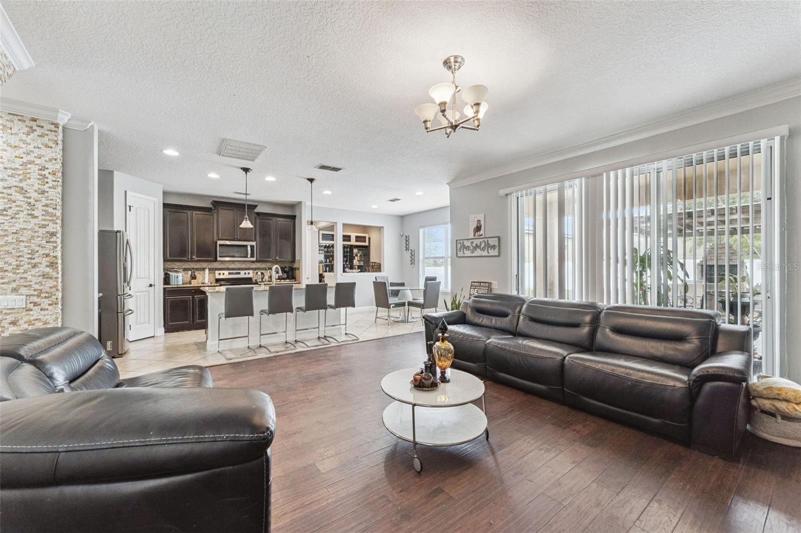 Open-plan living room with dark leather sofas, wood floors, and a kitchen breakfast bar.
