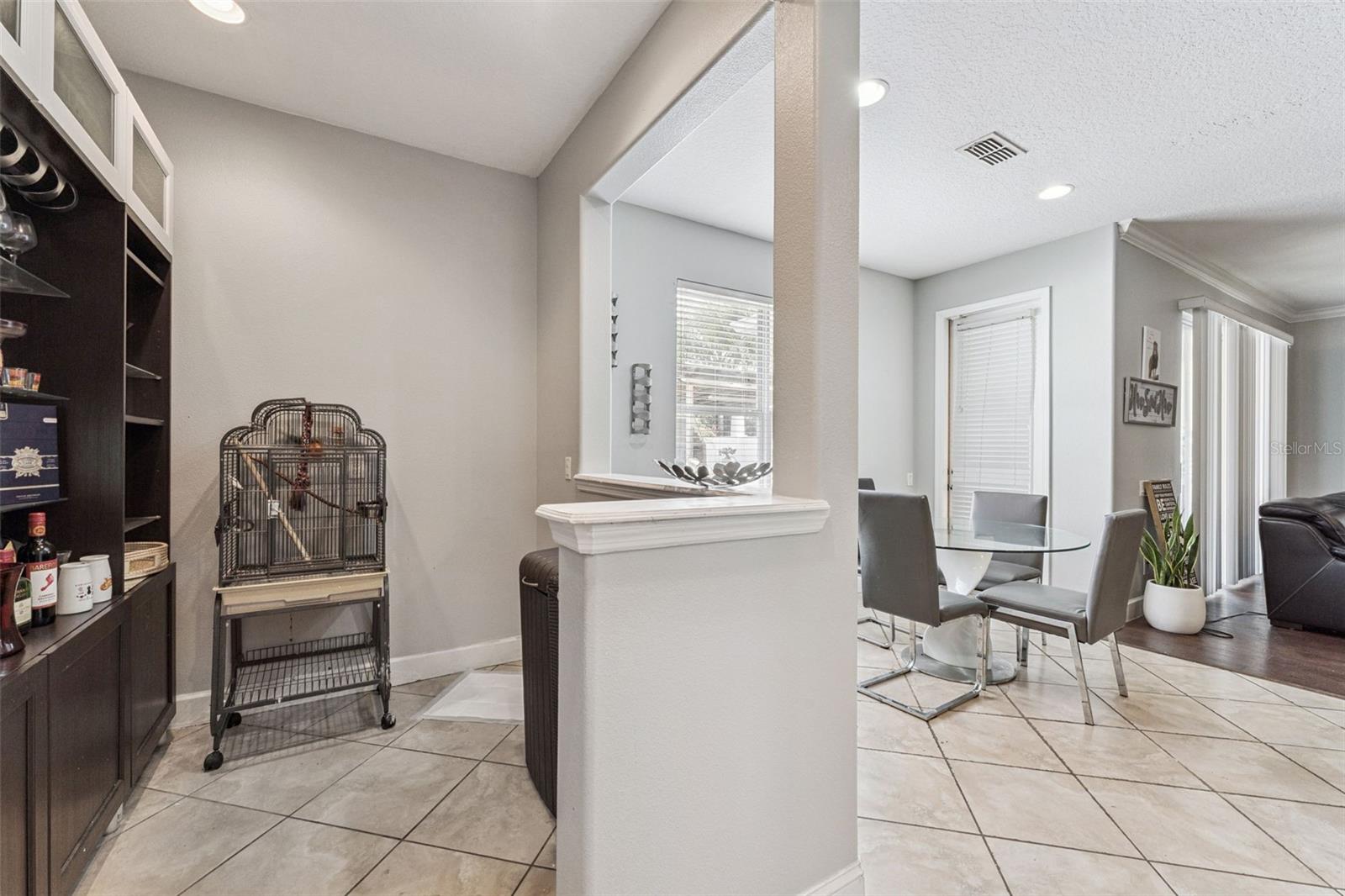 Dining area with a round glass table and gray chairs beside a built-in wine cabinet.