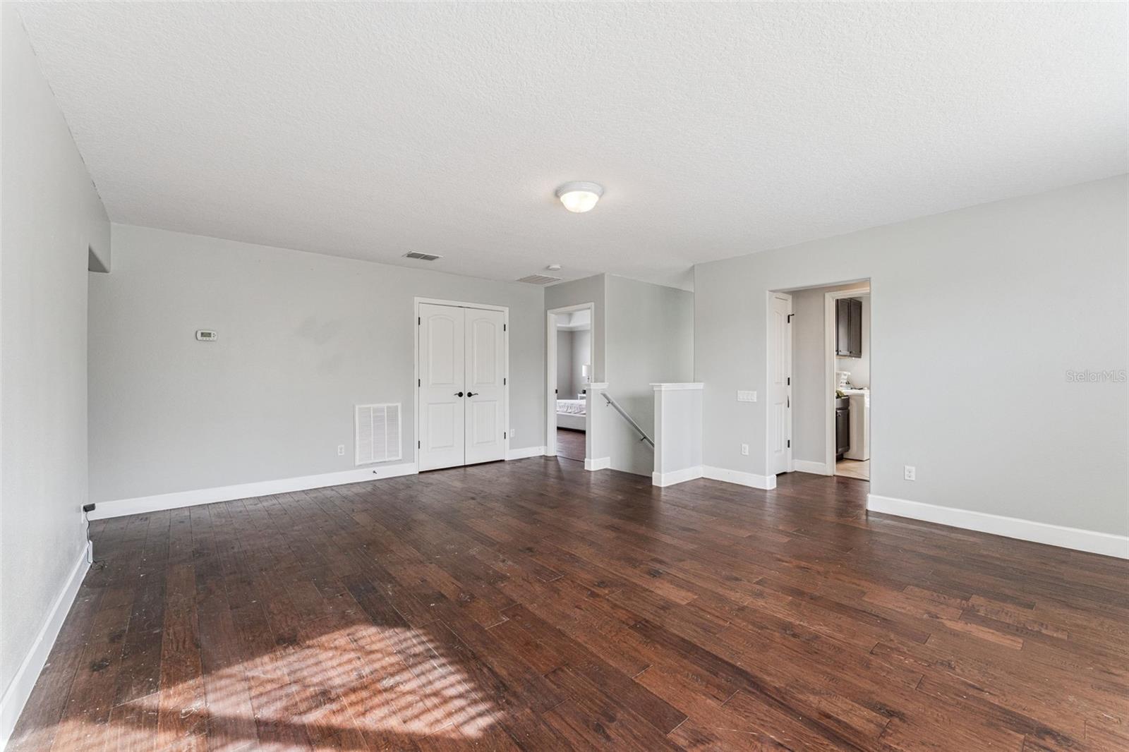 Empty room with dark hardwood floors, double closet doors, and doorways to adjoining spaces.