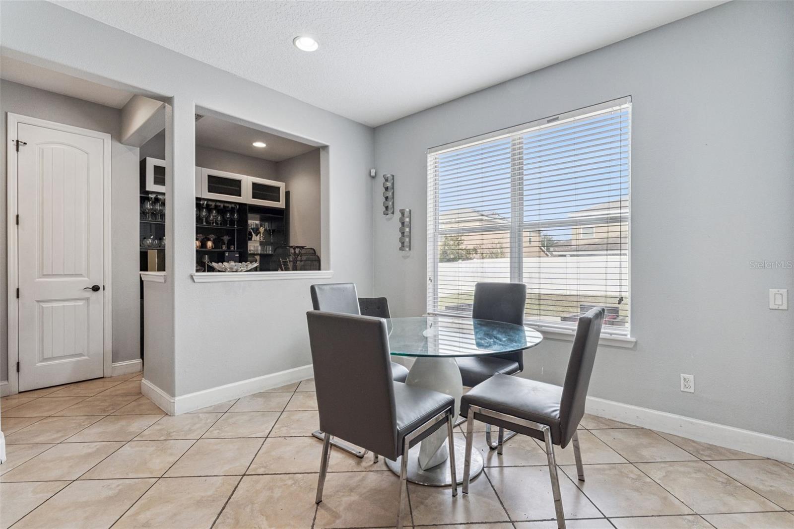 Dining area with a round glass table, tiled floor, and window overlooking a fenced yard.