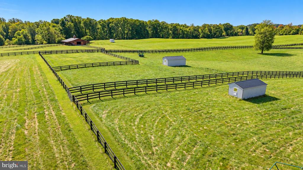 Aerial view of fenced green pastures with two metal sheds and a barn.