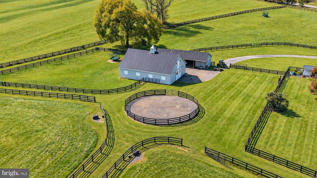 Aerial view of a horse property with a barn, fenced pastures, and a circular riding pen.