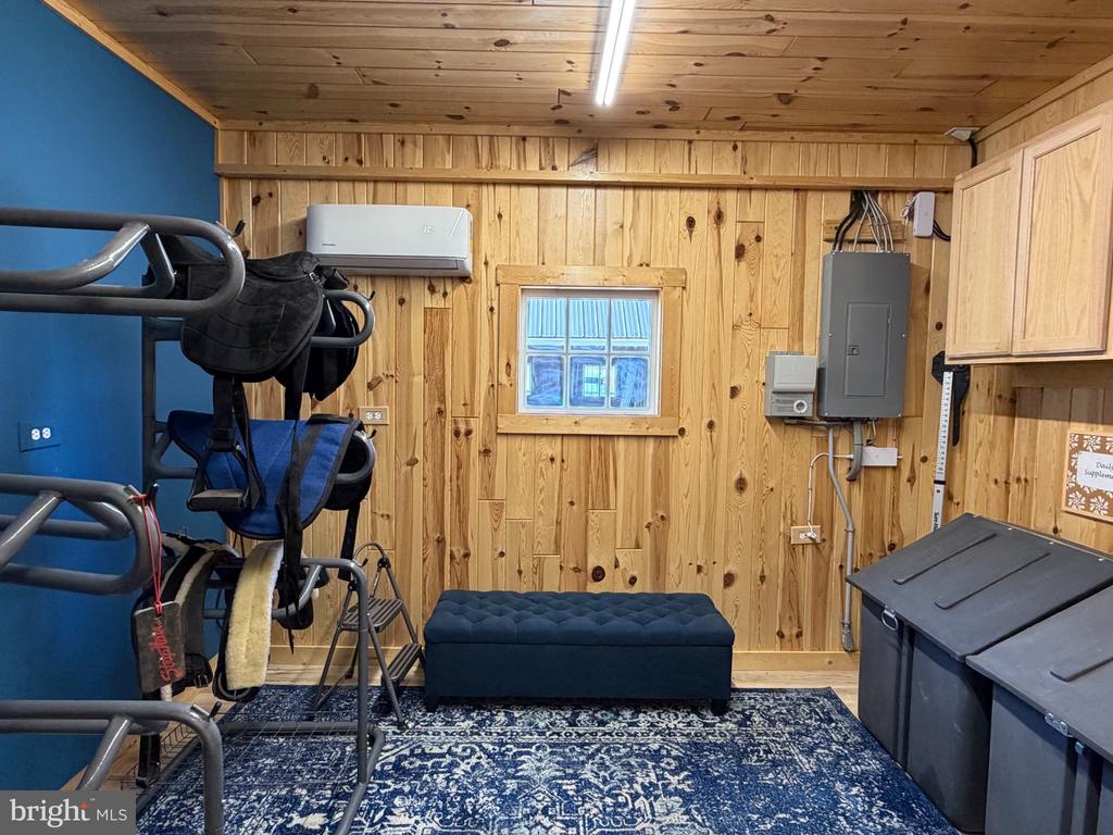 Wood-paneled tack room with saddles, riding equipment, a padded bench, and storage bins.