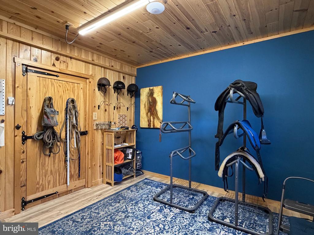 Equestrian tack room with saddles on racks, a wooden Dutch door, and blue walls.