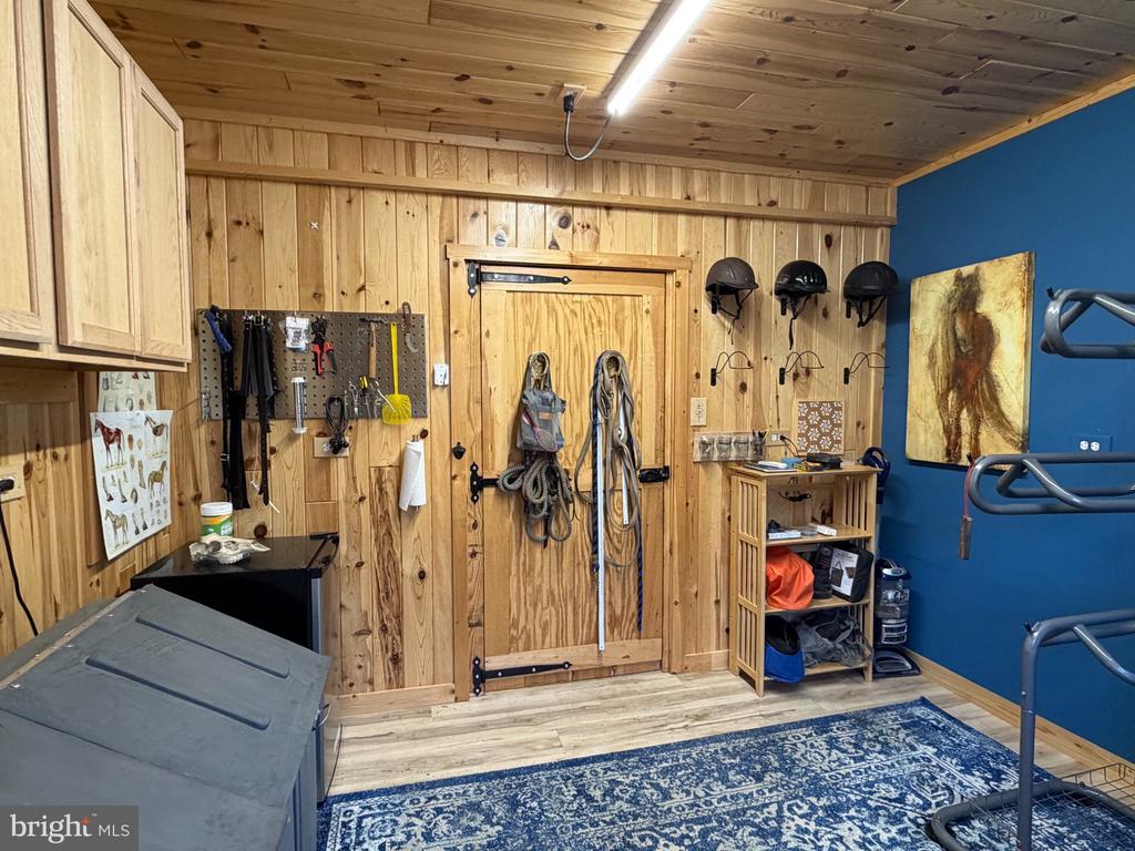 Wood-paneled tack room with hanging riding helmets and horse tack beside a blue accent wall.
