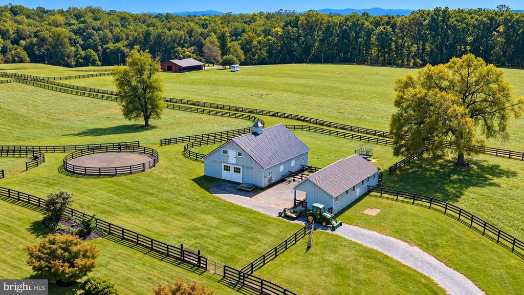 Aerial view of fenced horse paddocks, a round riding pen, and farm buildings amid green fields.