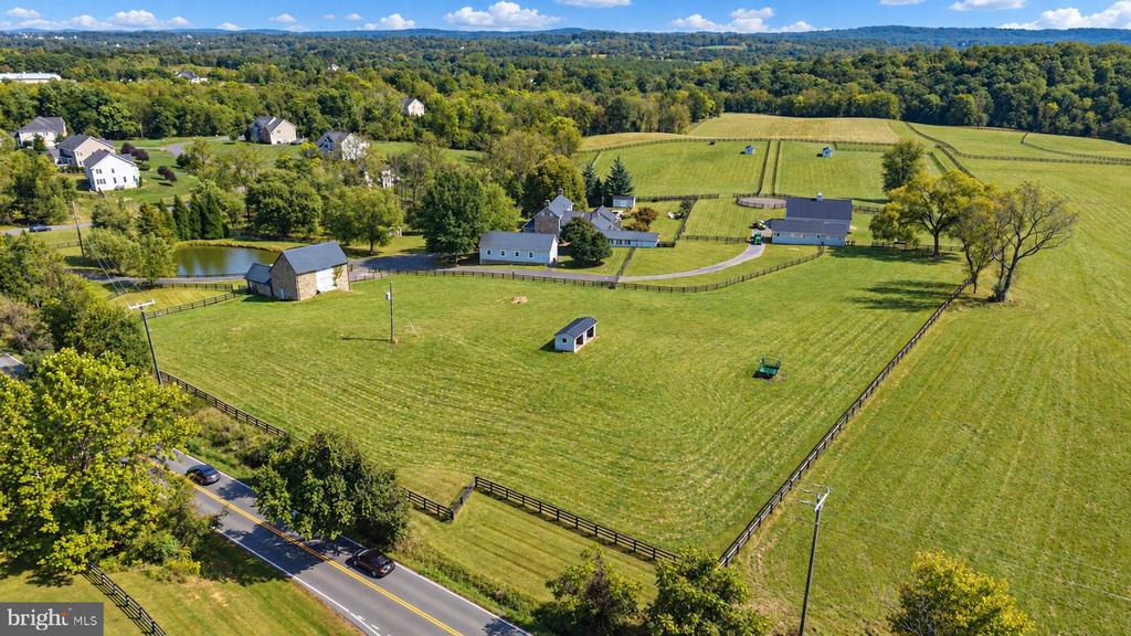 Aerial view of fenced green pastures, farm buildings, and a pond beside a road.