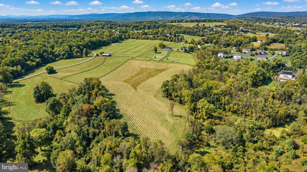 Aerial view of rolling fields and wooded acreage with scattered homes and a distant ridge.