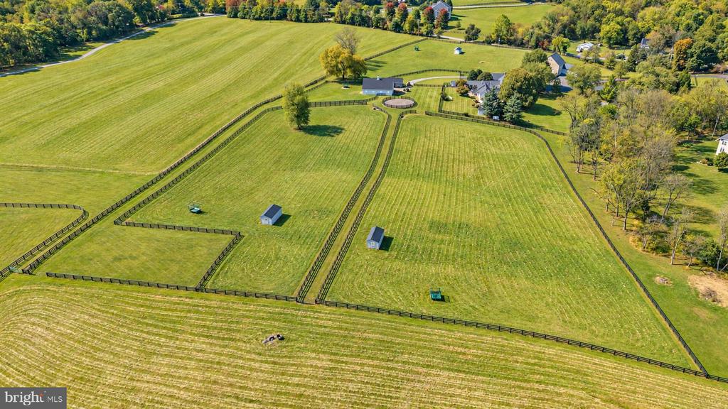 Aerial view of fenced pastureland with small outbuildings and a residence among autumn trees.