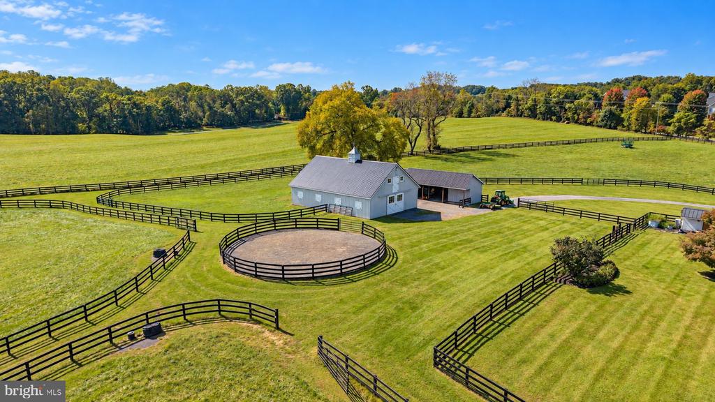 Aerial view of a horse farm with fenced pastures, a barn, and a round riding pen.