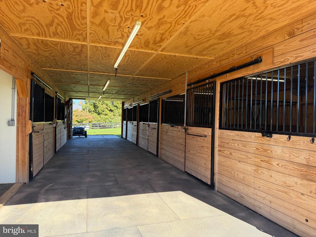 Horse stable aisle with wooden stalls and black metal bars on both sides.
